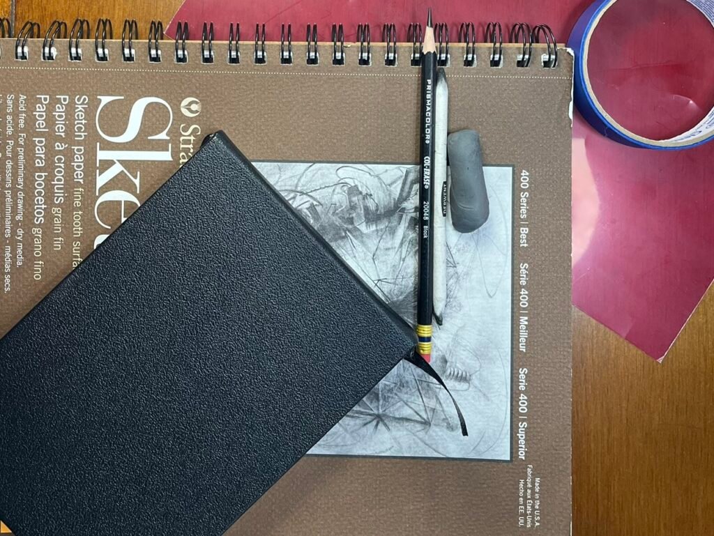 A STrathmore drawing book, black sketchbook, pencil, kneaded eraser, red acetate and masking tape