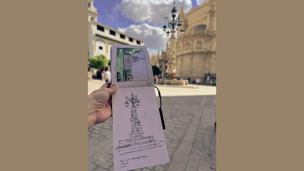 Sketchbook held open in Plaza de la Virgen de los Reyes, Seville, showing fountain sketch with cathedral in background