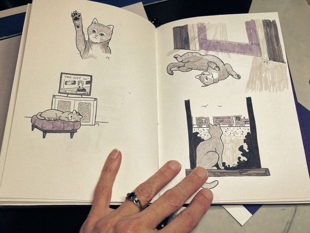 Open sketchbook showing grayscale illustrations of a cat in various relaxed or disinterested poses, including watching a circus train and ignoring dramatic news.