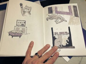Open sketchbook showing grayscale illustrations of a cat in various relaxed or disinterested poses, including watching a circus train and ignoring dramatic news.