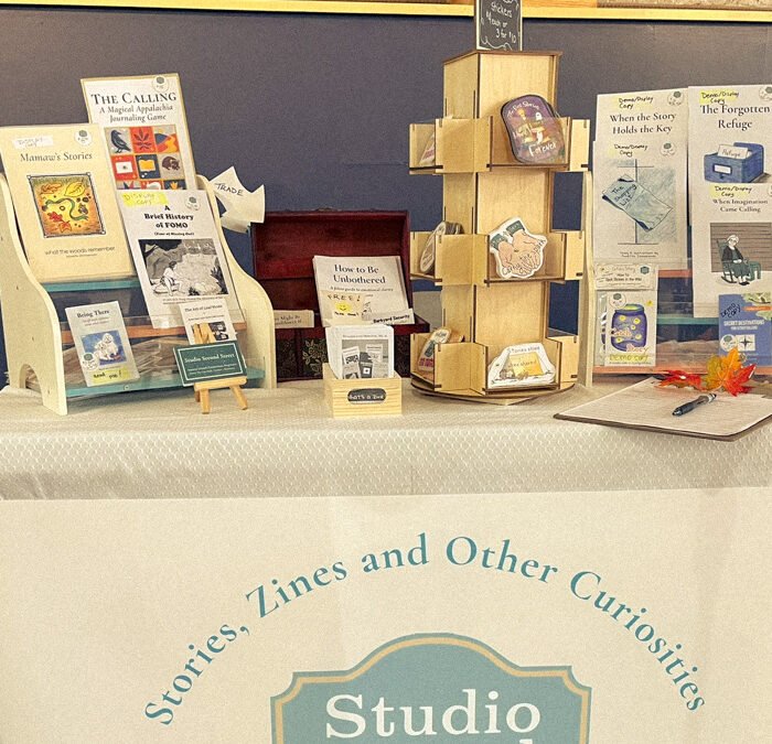 Studio Second Street zine display at Johnson City Zine Fest, set against white brick wall.