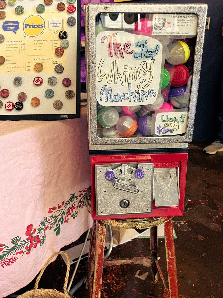 Retro vending machine labeled ‘The Whimsy Machine,’ filled with toy capsules of mini zines and stickers.