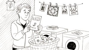 A black-and-white illustration of a woman standing in a laundry room, holding up a zine with a thoughtful expression as if examining a shirt. A laundry basket in front of her is filled with zines, short stories, and creative papers. Behind her, more artwork and small illustrations hang from a clothesline above a washing machine and dryer.