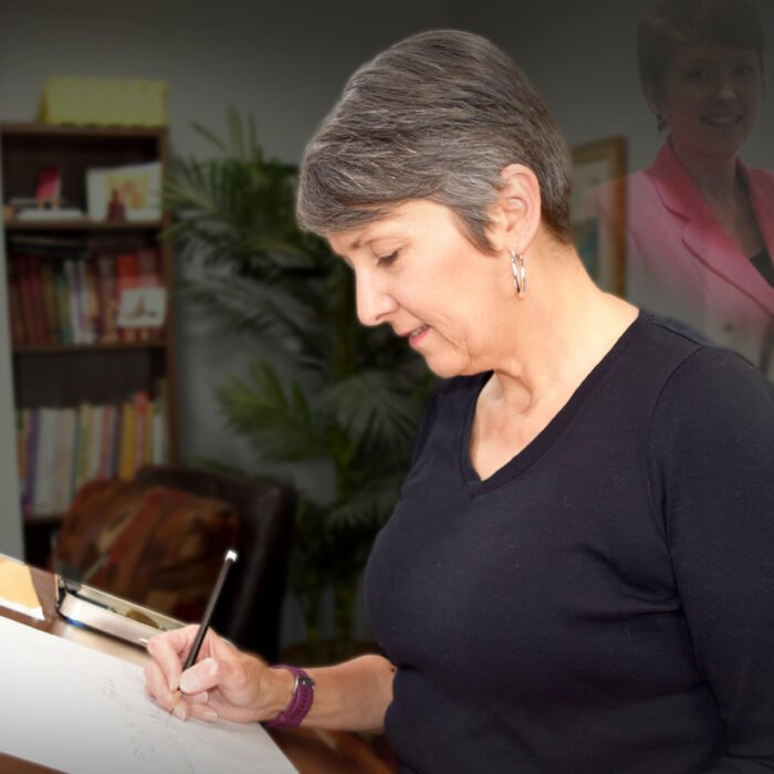 Woman drawing at a desk in a home studio, with a faint, ghosted image of her younger self in the background.