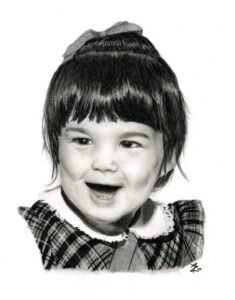 Graphite and charcoal portrait of a smiling two-year-old girl with dark hair, a bow, and a plaid dress.