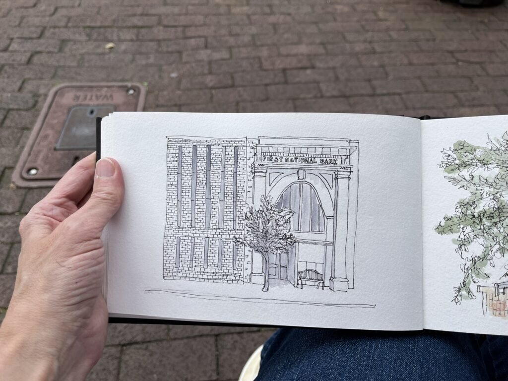 Ink sketchbook drawing of the First National Bank building in Jonesborough, shown with brick details, arched entrance, tree, bench, and sidewalk.