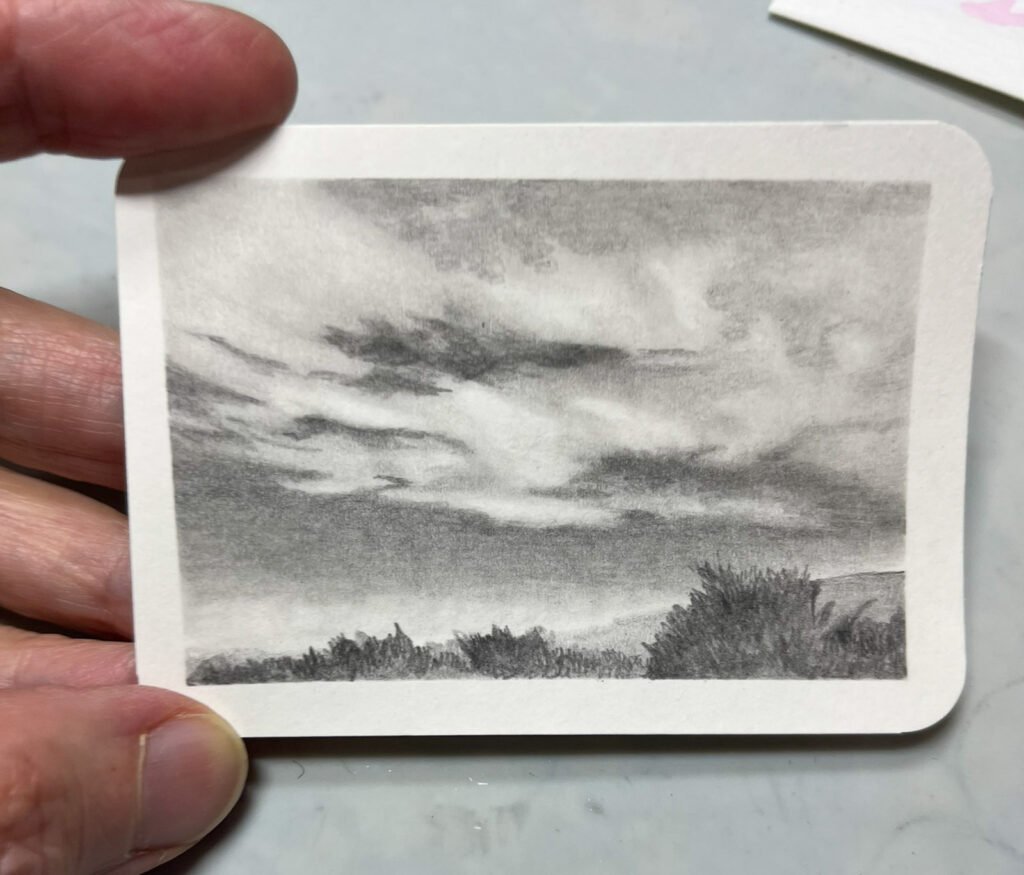 A small graphite drawing of layered clouds over a low landscape.