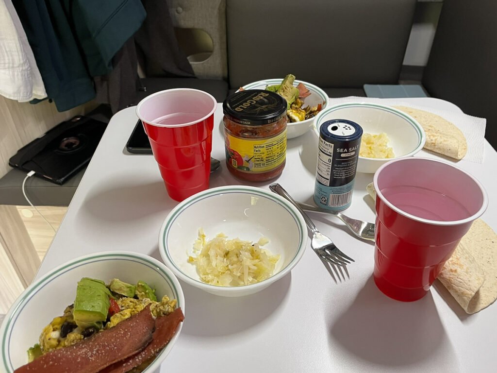 Breakfast bowls, tortillas, salsa, sauerkraut, seasonings, and red cups arranged on the table inside the trailer.