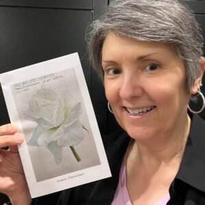 A smiling woman holds up a printed copy of the Realmscapes Dispatch zine, titled “Small Experiments, Larger Efforts,” featuring a pale watercolor flower on the cover.