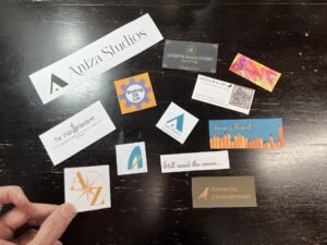 A hand holds an old Aniza logo card above a dark wooden table scattered with business cards and logos from ten years of creative projects and blogs.
