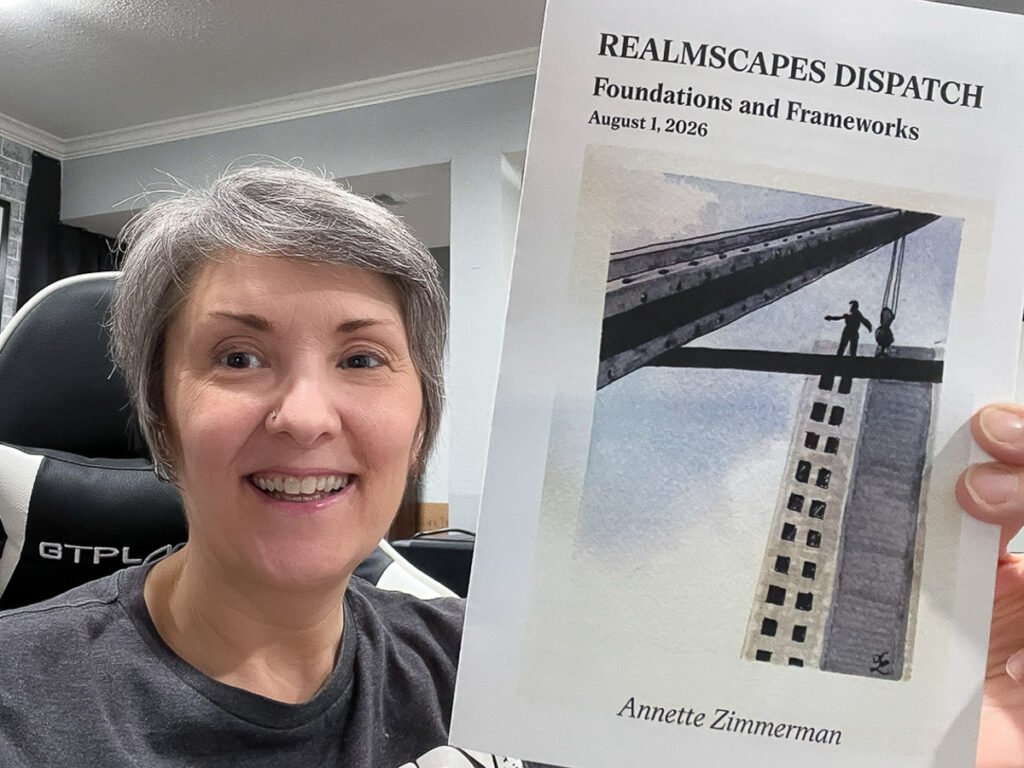Anni Zimmerman smiles while holding the August 2026 Realmscapes Dispatch newsletter, titled “Foundations and Frameworks,” featuring an illustration of a person standing on a steel beam above a skyscraper.