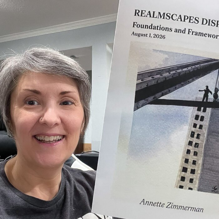 Anni Zimmerman smiles while holding the August 2026 Realmscapes Dispatch newsletter, titled “Foundations and Frameworks,” featuring an illustration of a person standing on a steel beam above a skyscraper.