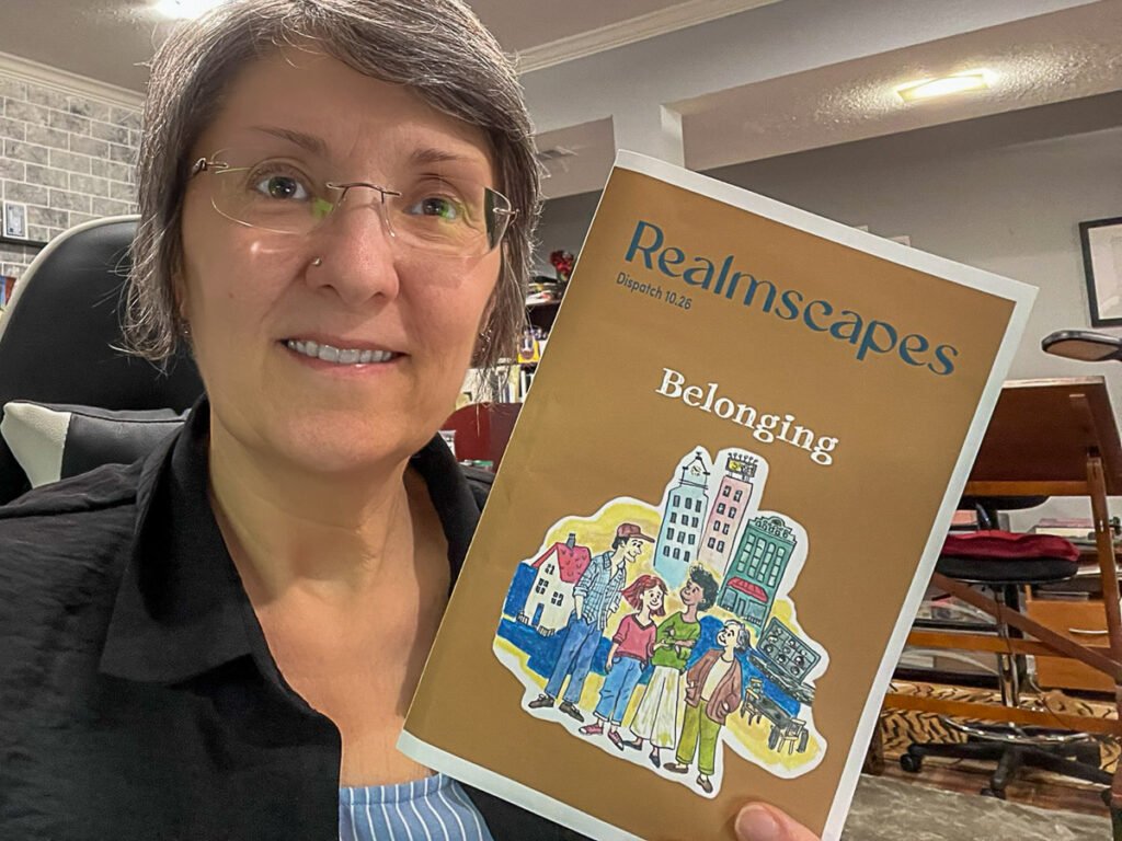 Anni holds up a copy of her new dispatch, a gold color cover titled "Belonging'